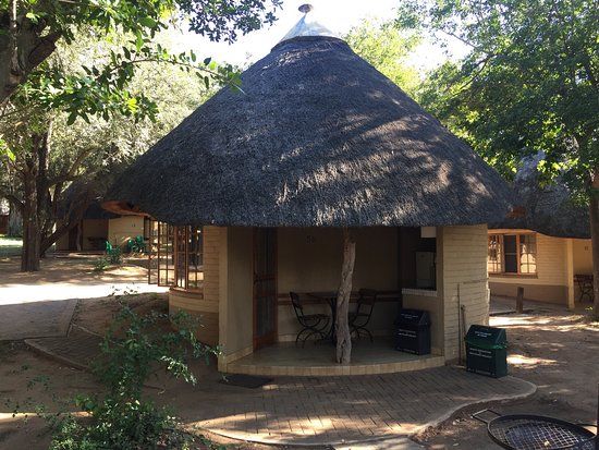A thatched SANParks bungalow among trees in Skukuza Camp.